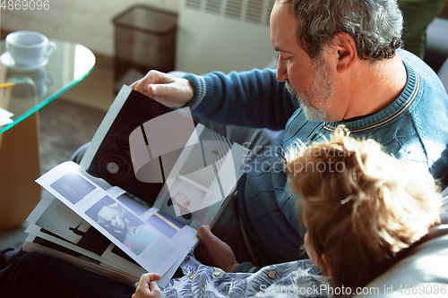 Image of Grandfather and his grandson spending time insulated at home, having fun, reading magazine together, happy