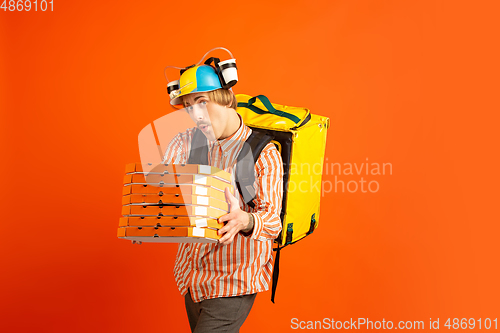 Image of Contacless delivery service during quarantine. Man delivers food and shopping bags during insulation. Emotions of deliveryman isolated on orange background.