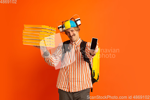 Image of Contacless delivery service during quarantine. Man delivers food and shopping bags during insulation. Emotions of deliveryman isolated on orange background.