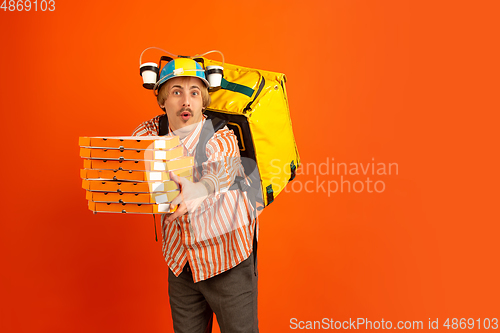 Image of Contacless delivery service during quarantine. Man delivers food and shopping bags during insulation. Emotions of deliveryman isolated on orange background.