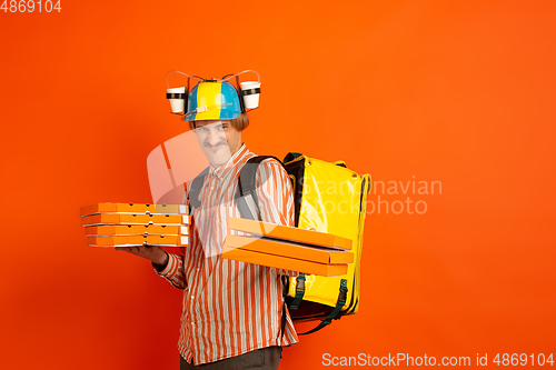 Image of Contacless delivery service during quarantine. Man delivers food and shopping bags during insulation. Emotions of deliveryman isolated on orange background.