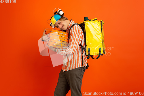 Image of Contacless delivery service during quarantine. Man delivers food and shopping bags during insulation. Emotions of deliveryman isolated on orange background.