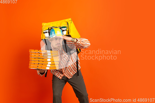 Image of Contacless delivery service during quarantine. Man delivers food and shopping bags during insulation. Emotions of deliveryman isolated on orange background.