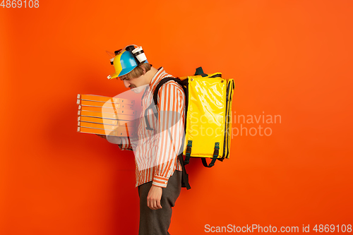 Image of Contacless delivery service during quarantine. Man delivers food and shopping bags during insulation. Emotions of deliveryman isolated on orange background.