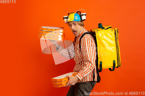 Image of Contacless delivery service during quarantine. Man delivers food and shopping bags during insulation. Emotions of deliveryman isolated on orange background.