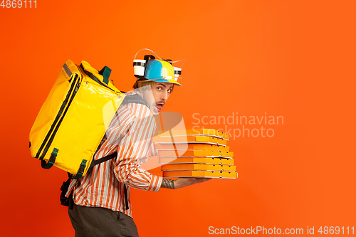 Image of Contacless delivery service during quarantine. Man delivers food and shopping bags during insulation. Emotions of deliveryman isolated on orange background.