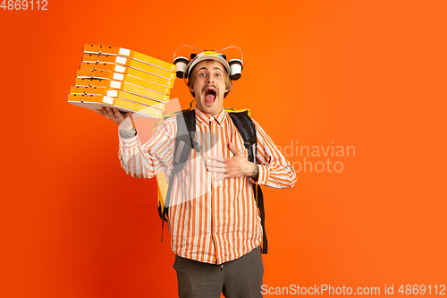 Image of Contacless delivery service during quarantine. Man delivers food and shopping bags during insulation. Emotions of deliveryman isolated on orange background.