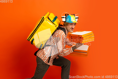 Image of Contacless delivery service during quarantine. Man delivers food and shopping bags during insulation. Emotions of deliveryman isolated on orange background.