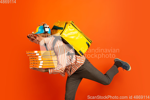 Image of Contacless delivery service during quarantine. Man delivers food and shopping bags during insulation. Emotions of deliveryman isolated on orange background.