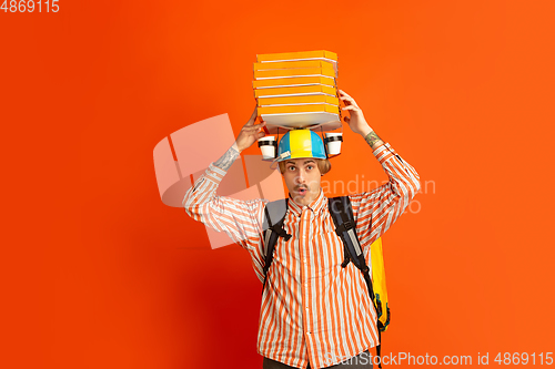 Image of Contacless delivery service during quarantine. Man delivers food and shopping bags during insulation. Emotions of deliveryman isolated on orange background.