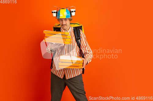 Image of Contacless delivery service during quarantine. Man delivers food and shopping bags during insulation. Emotions of deliveryman isolated on orange background.