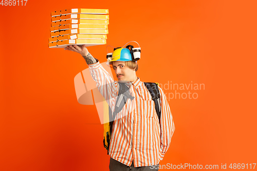 Image of Contacless delivery service during quarantine. Man delivers food and shopping bags during insulation. Emotions of deliveryman isolated on orange background.