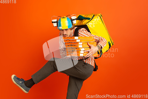 Image of Contacless delivery service during quarantine. Man delivers food and shopping bags during insulation. Emotions of deliveryman isolated on orange background.