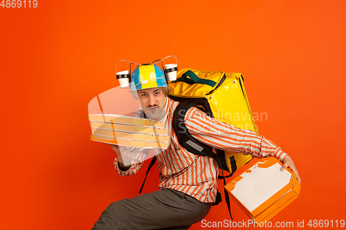 Image of Contacless delivery service during quarantine. Man delivers food and shopping bags during insulation. Emotions of deliveryman isolated on orange background.