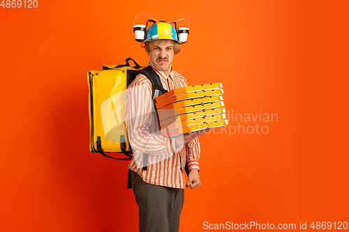 Image of Contacless delivery service during quarantine. Man delivers food and shopping bags during insulation. Emotions of deliveryman isolated on orange background.