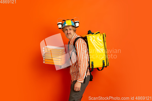 Image of Contacless delivery service during quarantine. Man delivers food and shopping bags during insulation. Emotions of deliveryman isolated on orange background.