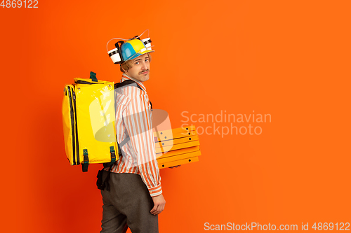 Image of Contacless delivery service during quarantine. Man delivers food and shopping bags during insulation. Emotions of deliveryman isolated on orange background.