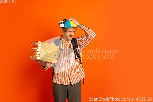 Image of Contacless delivery service during quarantine. Man delivers food and shopping bags during insulation. Emotions of deliveryman isolated on orange background.