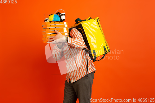 Image of Contacless delivery service during quarantine. Man delivers food and shopping bags during insulation. Emotions of deliveryman isolated on orange background.