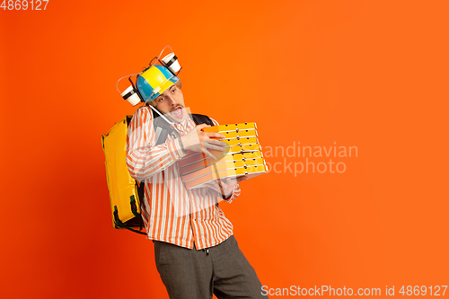 Image of Contacless delivery service during quarantine. Man delivers food and shopping bags during insulation. Emotions of deliveryman isolated on orange background.