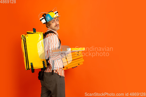 Image of Contacless delivery service during quarantine. Man delivers food and shopping bags during insulation. Emotions of deliveryman isolated on orange background.