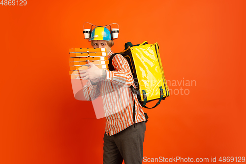 Image of Contacless delivery service during quarantine. Man delivers food and shopping bags during insulation. Emotions of deliveryman isolated on orange background.