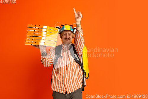 Image of Contacless delivery service during quarantine. Man delivers food and shopping bags during insulation. Emotions of deliveryman isolated on orange background.