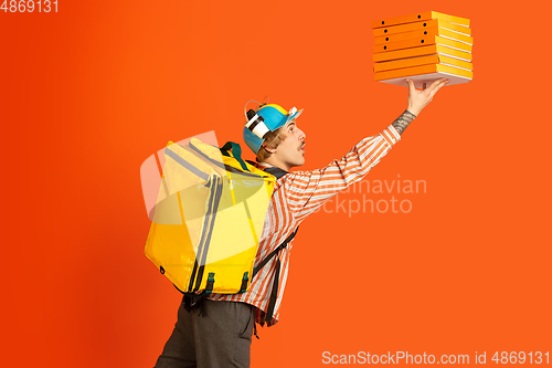 Image of Contacless delivery service during quarantine. Man delivers food and shopping bags during insulation. Emotions of deliveryman isolated on orange background.