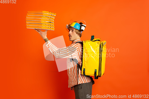 Image of Contacless delivery service during quarantine. Man delivers food and shopping bags during insulation. Emotions of deliveryman isolated on orange background.