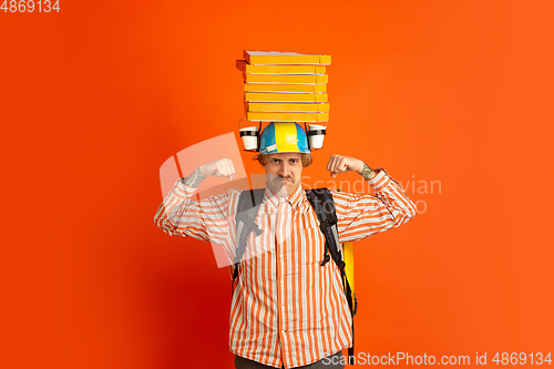 Image of Contacless delivery service during quarantine. Man delivers food and shopping bags during insulation. Emotions of deliveryman isolated on orange background.