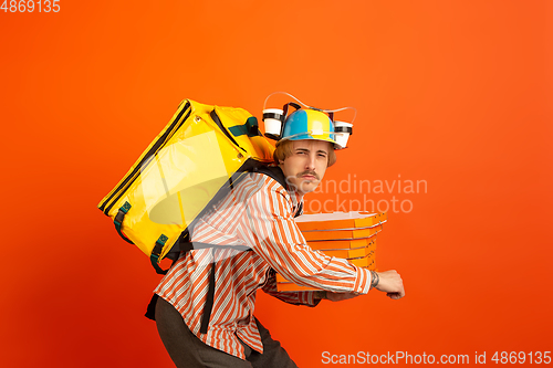 Image of Contacless delivery service during quarantine. Man delivers food and shopping bags during insulation. Emotions of deliveryman isolated on orange background.