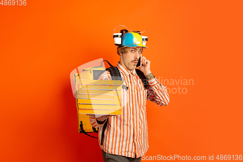 Image of Contacless delivery service during quarantine. Man delivers food and shopping bags during insulation. Emotions of deliveryman isolated on orange background.