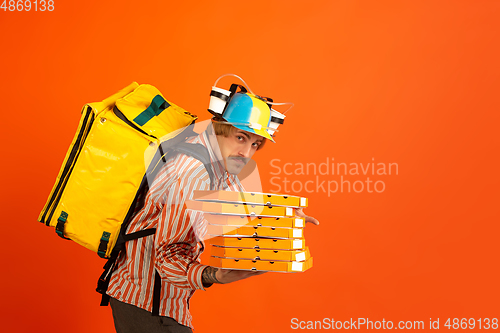 Image of Contacless delivery service during quarantine. Man delivers food and shopping bags during insulation. Emotions of deliveryman isolated on orange background.