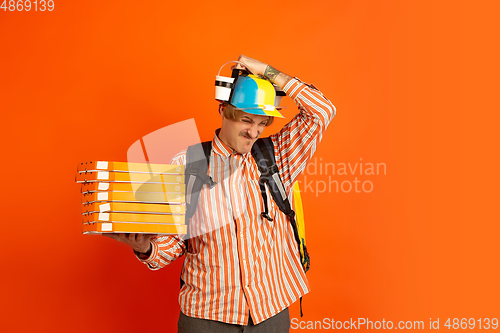 Image of Contacless delivery service during quarantine. Man delivers food and shopping bags during insulation. Emotions of deliveryman isolated on orange background.