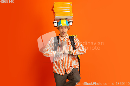 Image of Contacless delivery service during quarantine. Man delivers food and shopping bags during insulation. Emotions of deliveryman isolated on orange background.