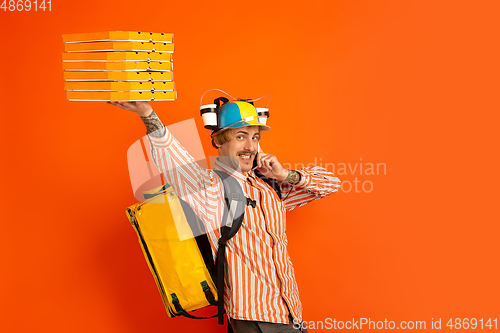 Image of Contacless delivery service during quarantine. Man delivers food and shopping bags during insulation. Emotions of deliveryman isolated on orange background.