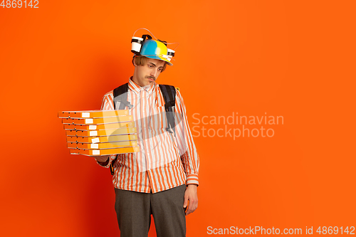 Image of Contacless delivery service during quarantine. Man delivers food and shopping bags during insulation. Emotions of deliveryman isolated on orange background.