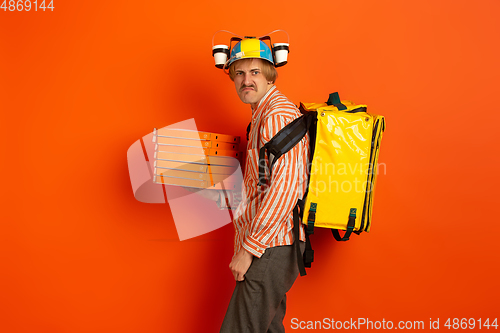 Image of Contacless delivery service during quarantine. Man delivers food and shopping bags during insulation. Emotions of deliveryman isolated on orange background.