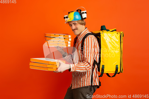 Image of Contacless delivery service during quarantine. Man delivers food and shopping bags during insulation. Emotions of deliveryman isolated on orange background.