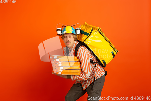 Image of Contacless delivery service during quarantine. Man delivers food and shopping bags during insulation. Emotions of deliveryman isolated on orange background.