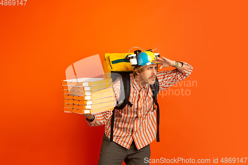 Image of Contacless delivery service during quarantine. Man delivers food and shopping bags during insulation. Emotions of deliveryman isolated on orange background.