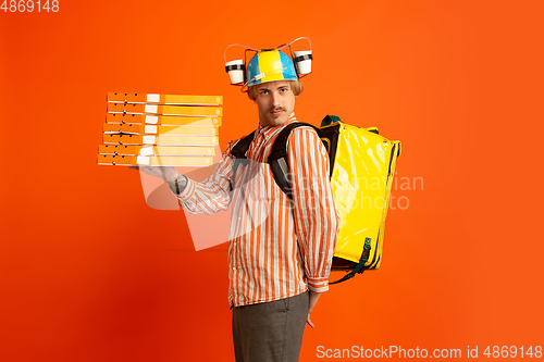 Image of Contacless delivery service during quarantine. Man delivers food and shopping bags during insulation. Emotions of deliveryman isolated on orange background.