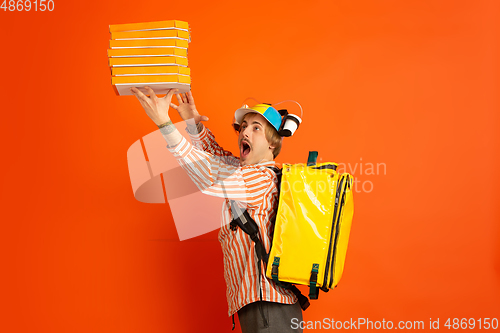 Image of Contacless delivery service during quarantine. Man delivers food and shopping bags during insulation. Emotions of deliveryman isolated on orange background.