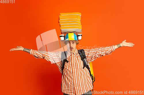 Image of Contacless delivery service during quarantine. Man delivers food and shopping bags during insulation. Emotions of deliveryman isolated on orange background.