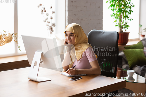 Image of A pretty young muslim woman at home during quarantine and self-insulation, remote working, shopping, studying, watching cinema