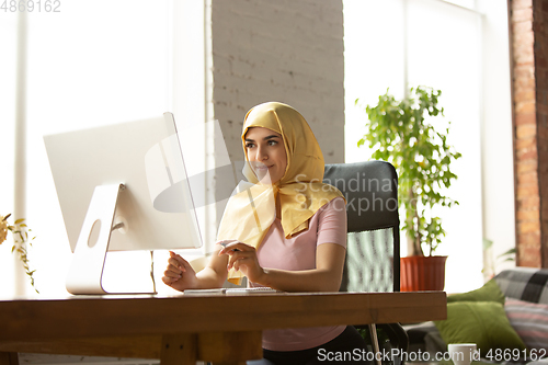 Image of A pretty young muslim woman at home during quarantine and self-insulation, remote working, shopping, studying, watching cinema