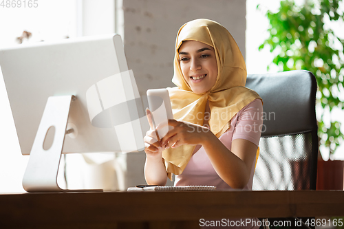 Image of A pretty young muslim woman at home during quarantine and self-insulation, remote working, shopping, studying, watching cinema