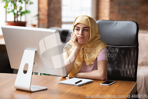 Image of A pretty young muslim woman at home during quarantine and self-insulation, remote working, shopping, studying, watching cinema