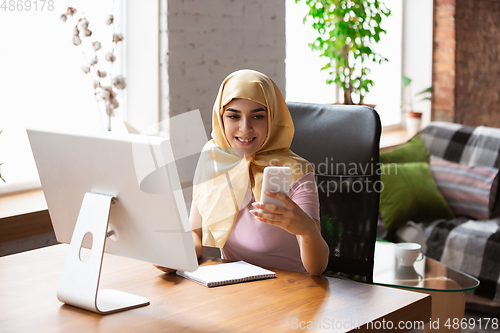 Image of A pretty young muslim woman at home during quarantine and self-insulation, remote working, shopping, studying, watching cinema