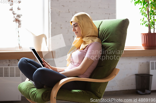 Image of A pretty young muslim woman at home during quarantine and self-insulation, using laptop for videocall, watching cinema, serials, shopping, studying